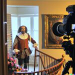 William Shakespeare in a 21st century house while he is being filmed by a video cameraman