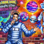 Graffiti art painting of Drake singing on a brick wall. In the background, the Drake Equation is depicted in a colorful, abstract way with stars